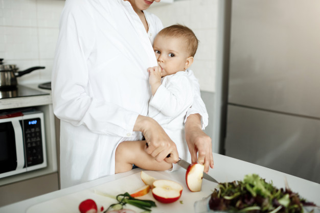 cropped-shot-mother-breastfeeding-her-baby-while-slicing-apple